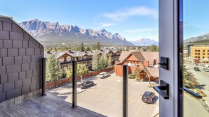 On peut admirer une vue sur la montagne depuis un balcon, avec en arrière-plan un parking et des immeubles.