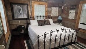 Um quarto aconchegante com cama, ventilador de teto, paredes de madeira, janela com cortinas e um quadro na parede.