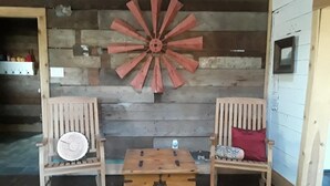 Quarto rústico com paredes de madeira, duas cadeiras de madeira com almofadas, um baú de madeira e uma grande decoração de moinho de vento de madeira.