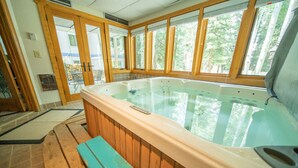 Ein Whirlpool mit Holzverkleidung, einer Holzbank und großen Fenstern mit Blick auf Bäume.