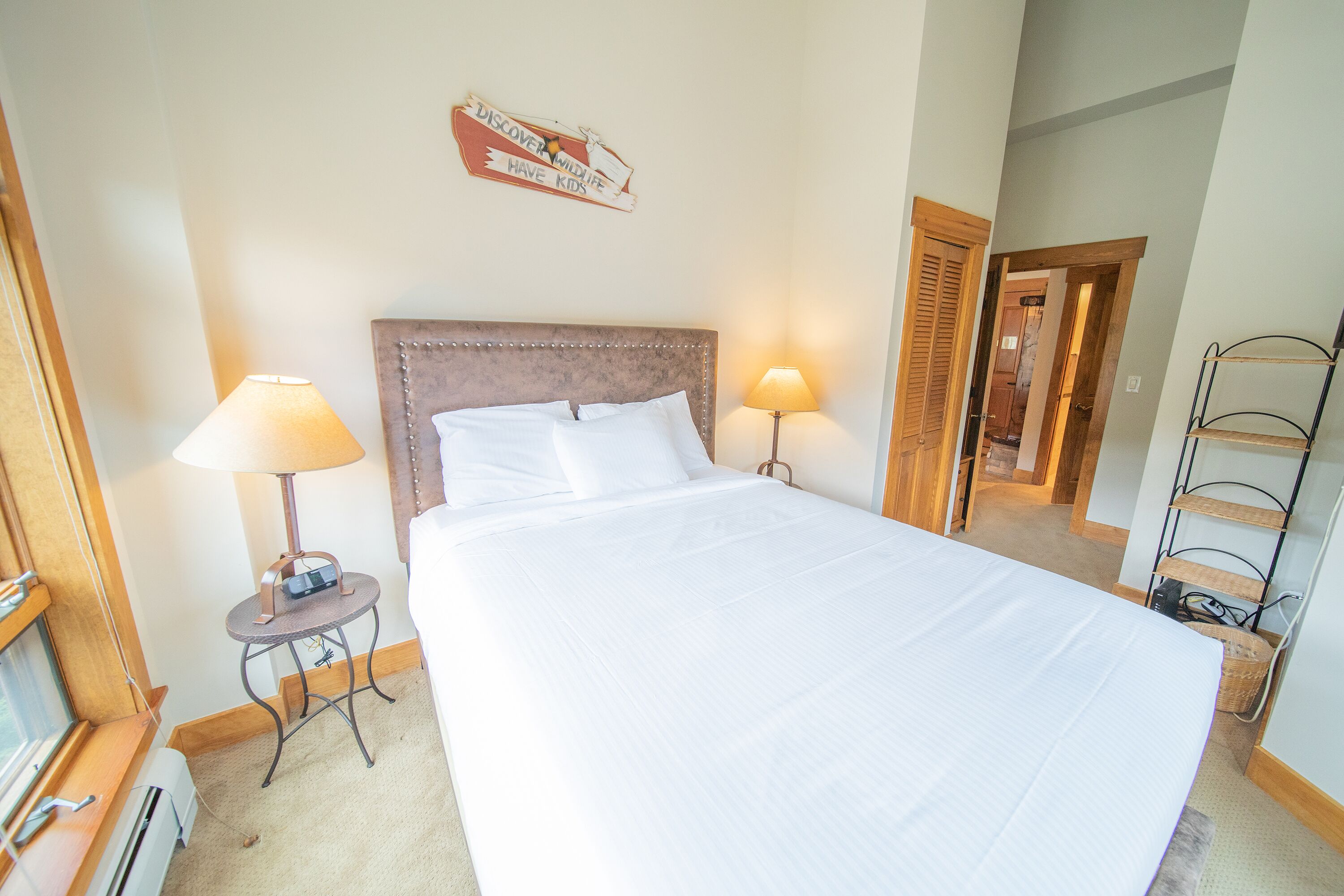 A neatly made bed with white linens, two bedside lamps, and a sign on the wall.
