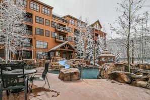 A snow-covered outdoor area with a pool, a slide, and a building with multiple balconies. - Springs 8911 (Keystone)