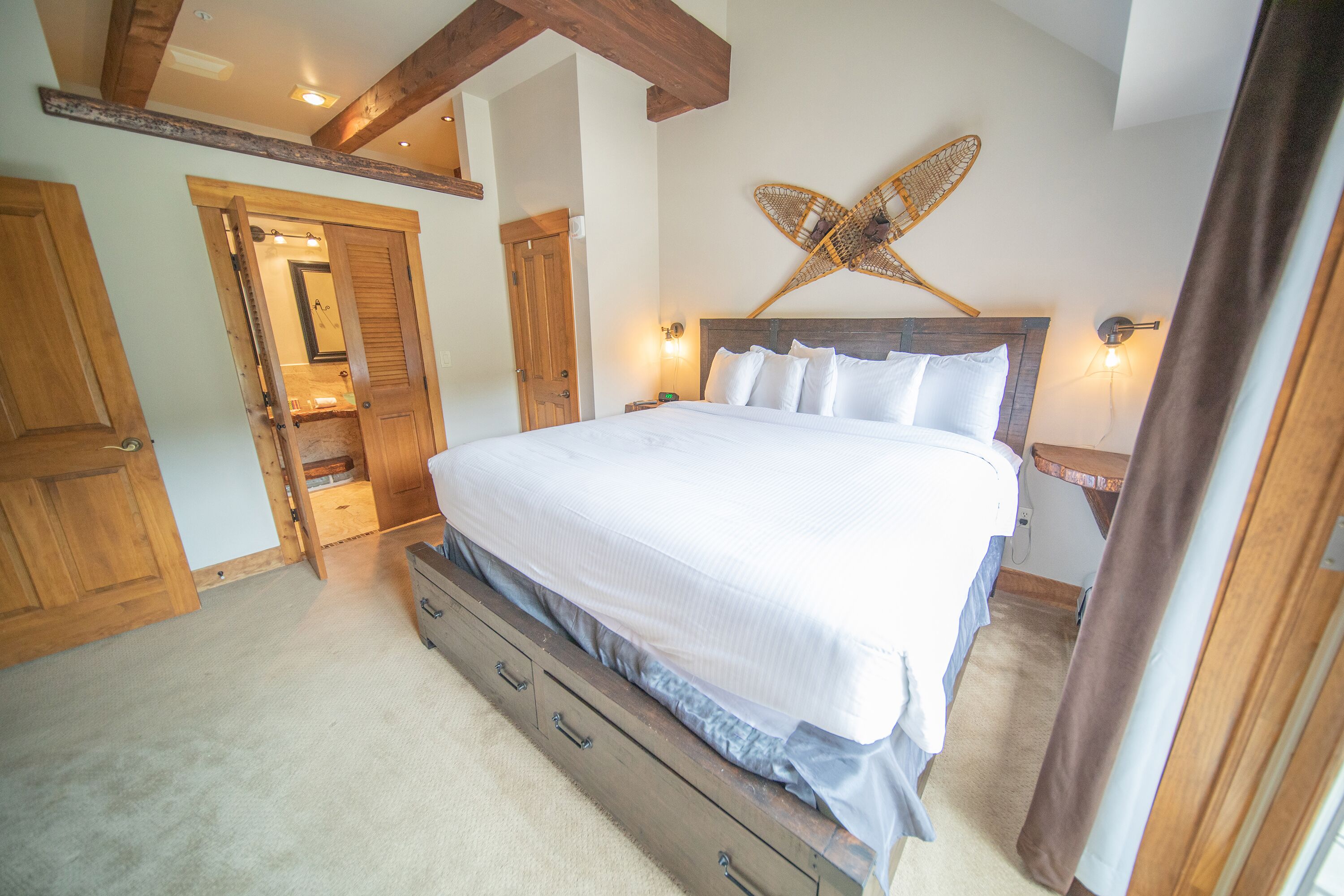 A bedroom with a wooden bed frame, a large window, and a wooden ceiling beam.