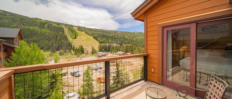 A balcony with a view of a mountainous landscape, a wooden building, and outdoor furniture.