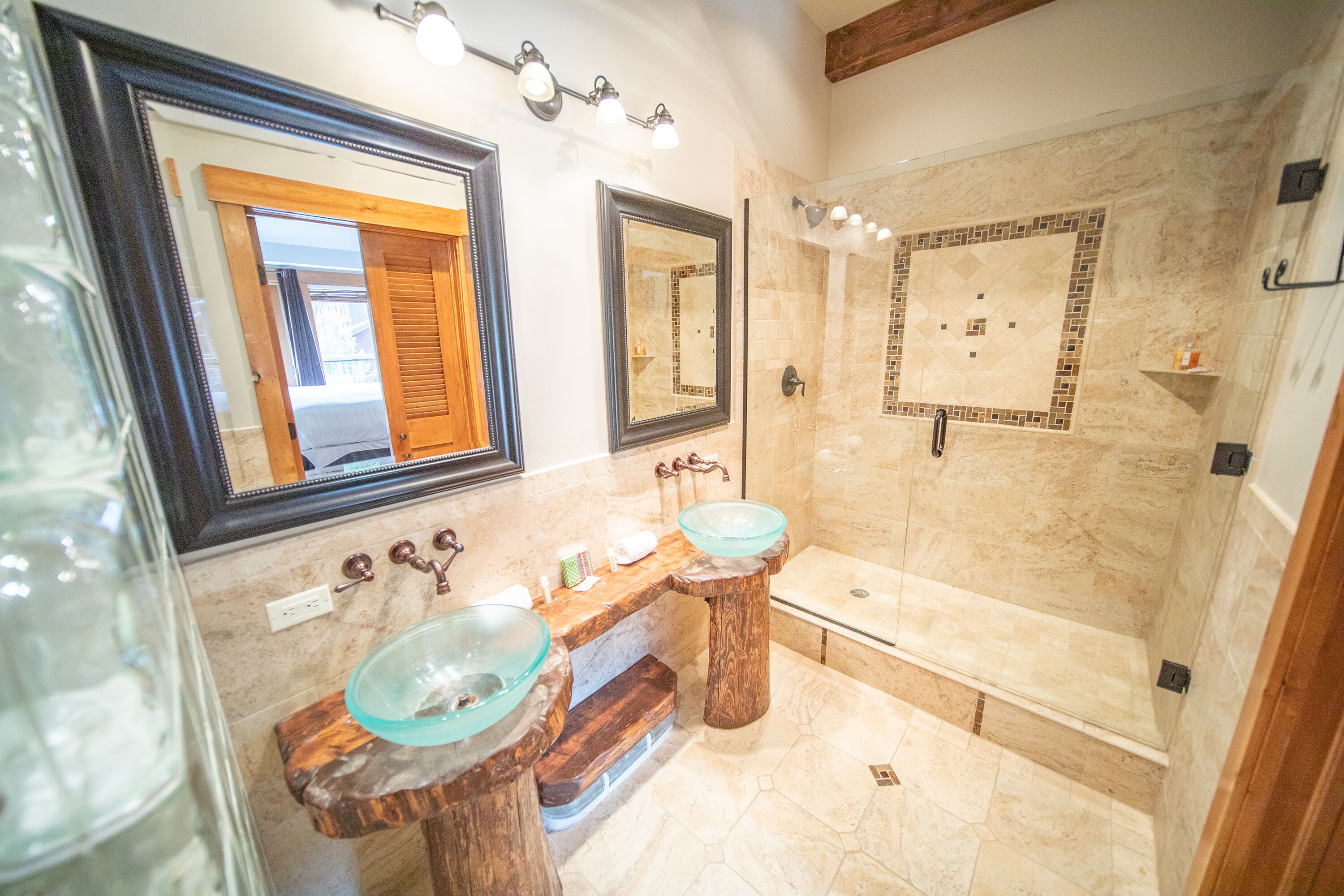 A bathroom with two glass sinks, a wooden vanity, a large mirror, and a tiled shower area.