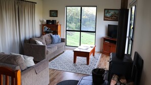 A living room with a sofa, a coffee table, a fireplace, a television, and a view of the outdoors.