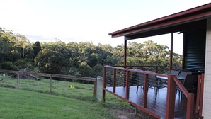 A wooden deck with outdoor seating, overlooking a grassy area and dense trees.