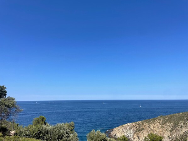 A coastal landscape with a clear sky, rocky terrain, and the sea.