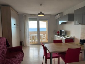 A modern kitchen with a dining area, a TV, and a view of the sea through the sliding glass door.