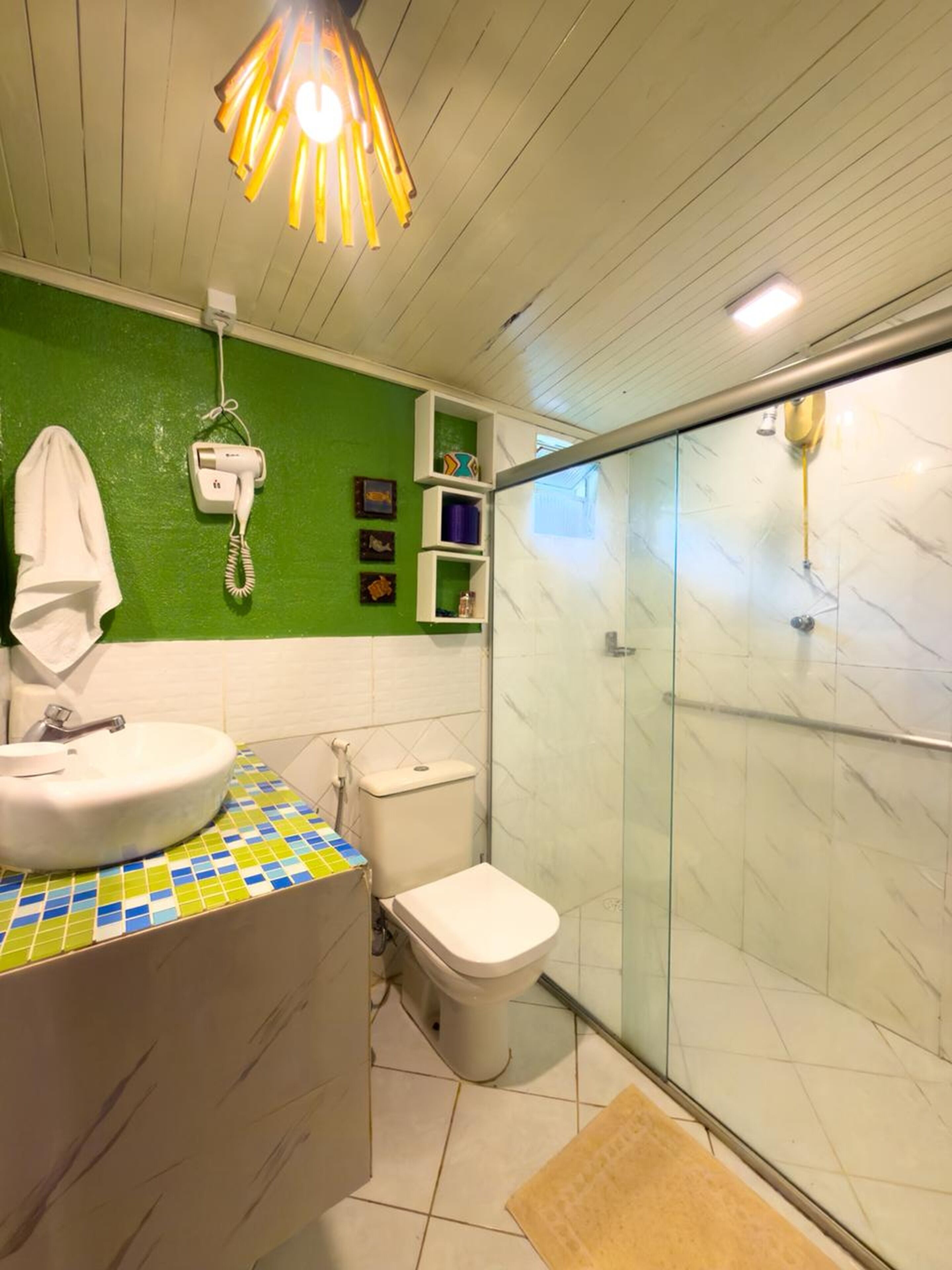 Een badkamer met een douchecabine van glas, een witte wastafel, een toilet en een haardroger aan de muur.