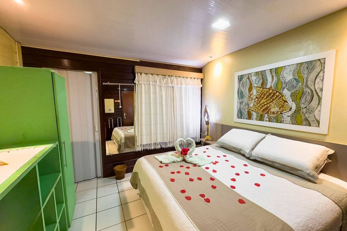 A hotel room with a bed, green wardrobe, and a painting on the wall.