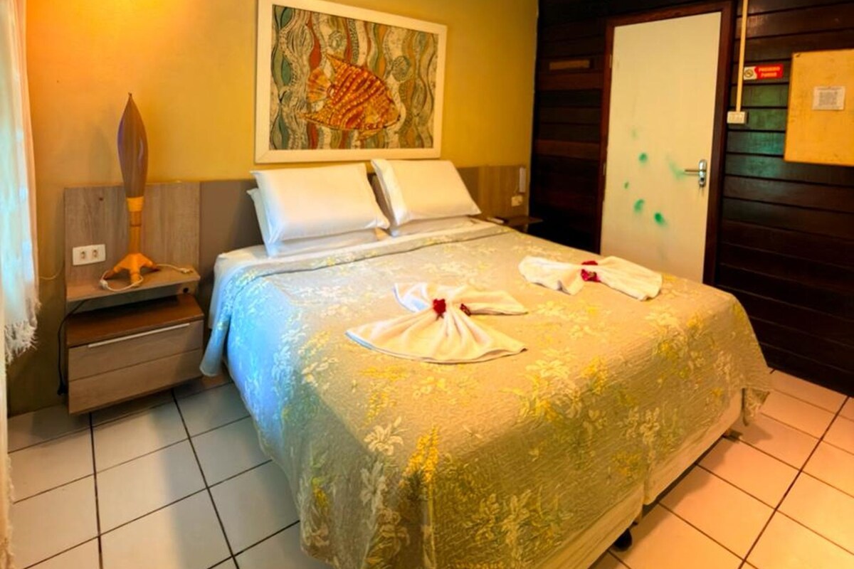 A hotel room with a bed, a nightstand, a lamp, a painting on the wall, and a door with a sign.