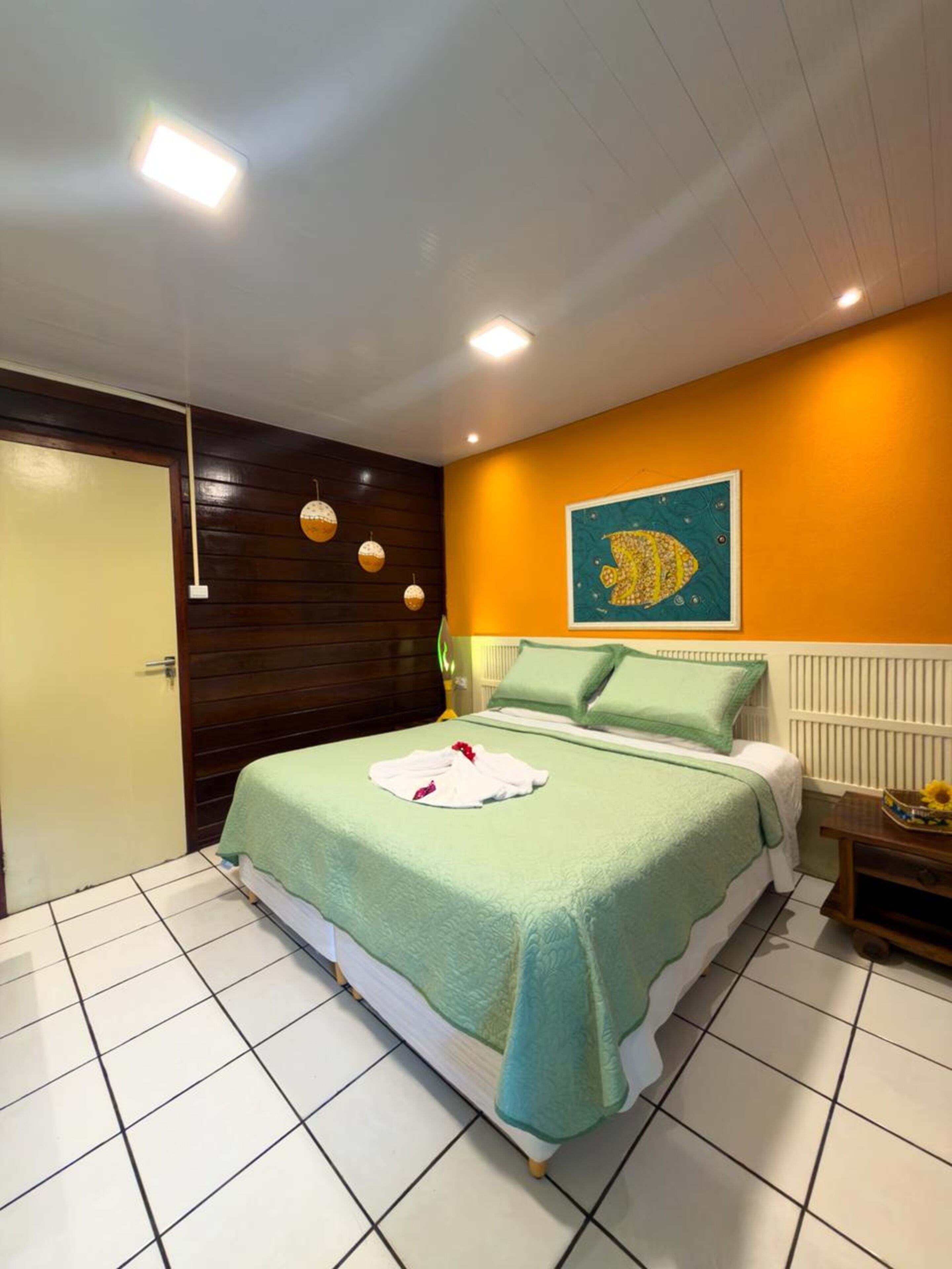 Quarto de hotel com cama, porta, parede com pintura e chão de azulejos.