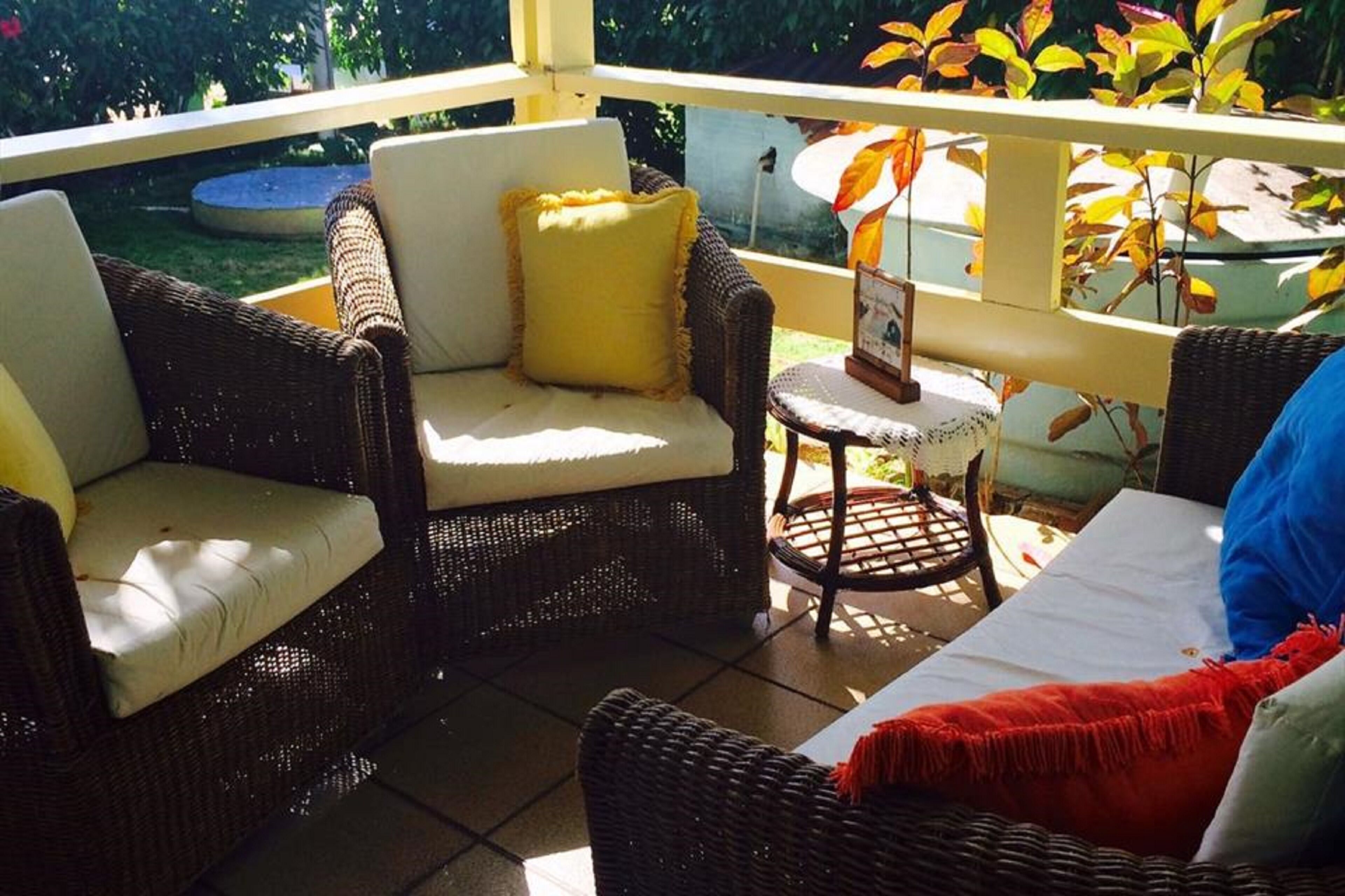 A covered patio area with wicker furniture, including two chairs and a small table, and a view of a garden with autumn foliage.