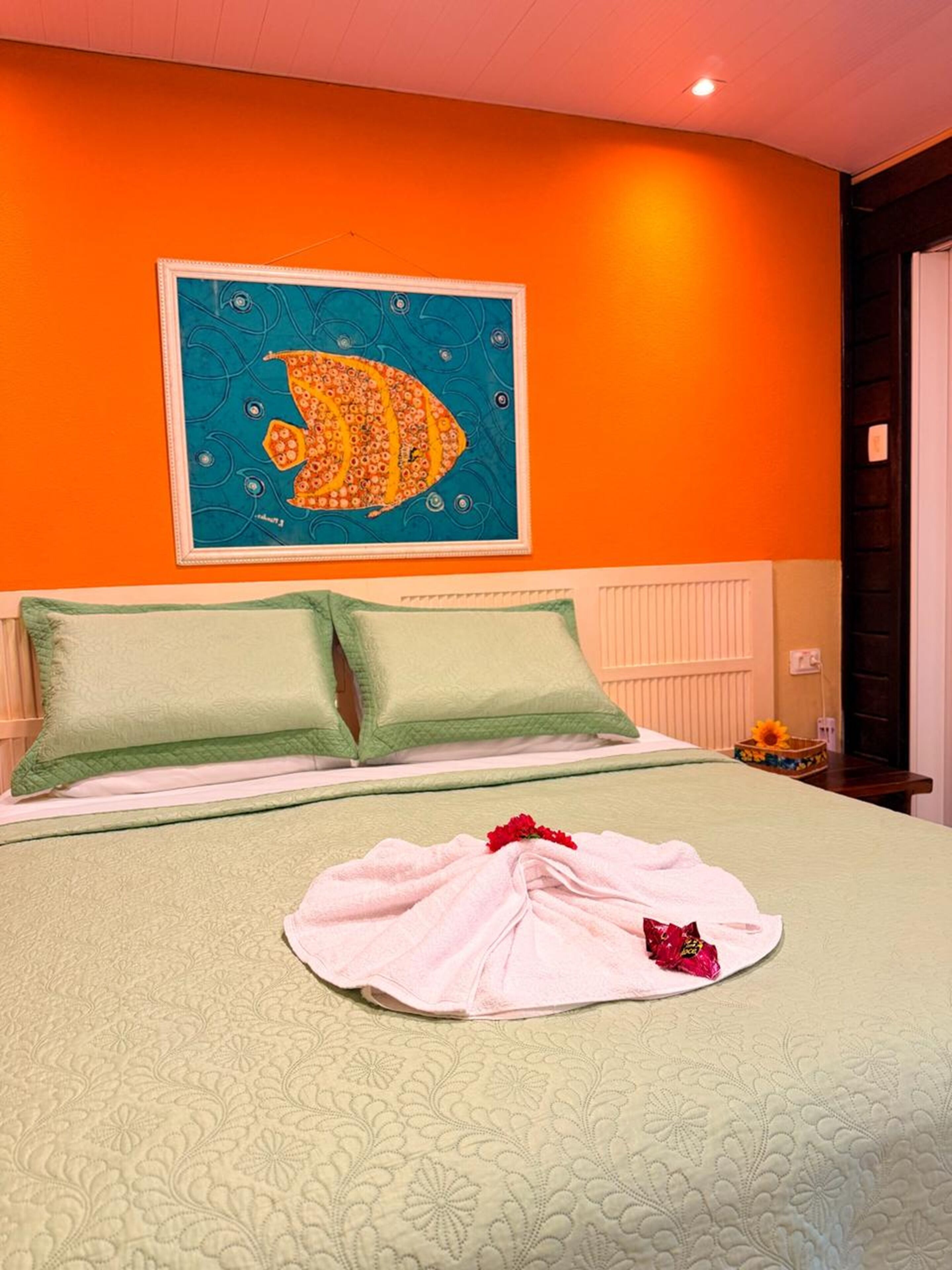 Hotelkamer met een bed, groene kussens, een blauwgroene muur met kleurrijke kunst en een witte handdoek op het bed.