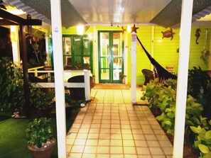Katettu ulkoalue, jolta laatoitettu käytävä johtaa vihreään oveen. Alueen ympärillä on ruukuissa olevia kasveja ja tähtikoriste.