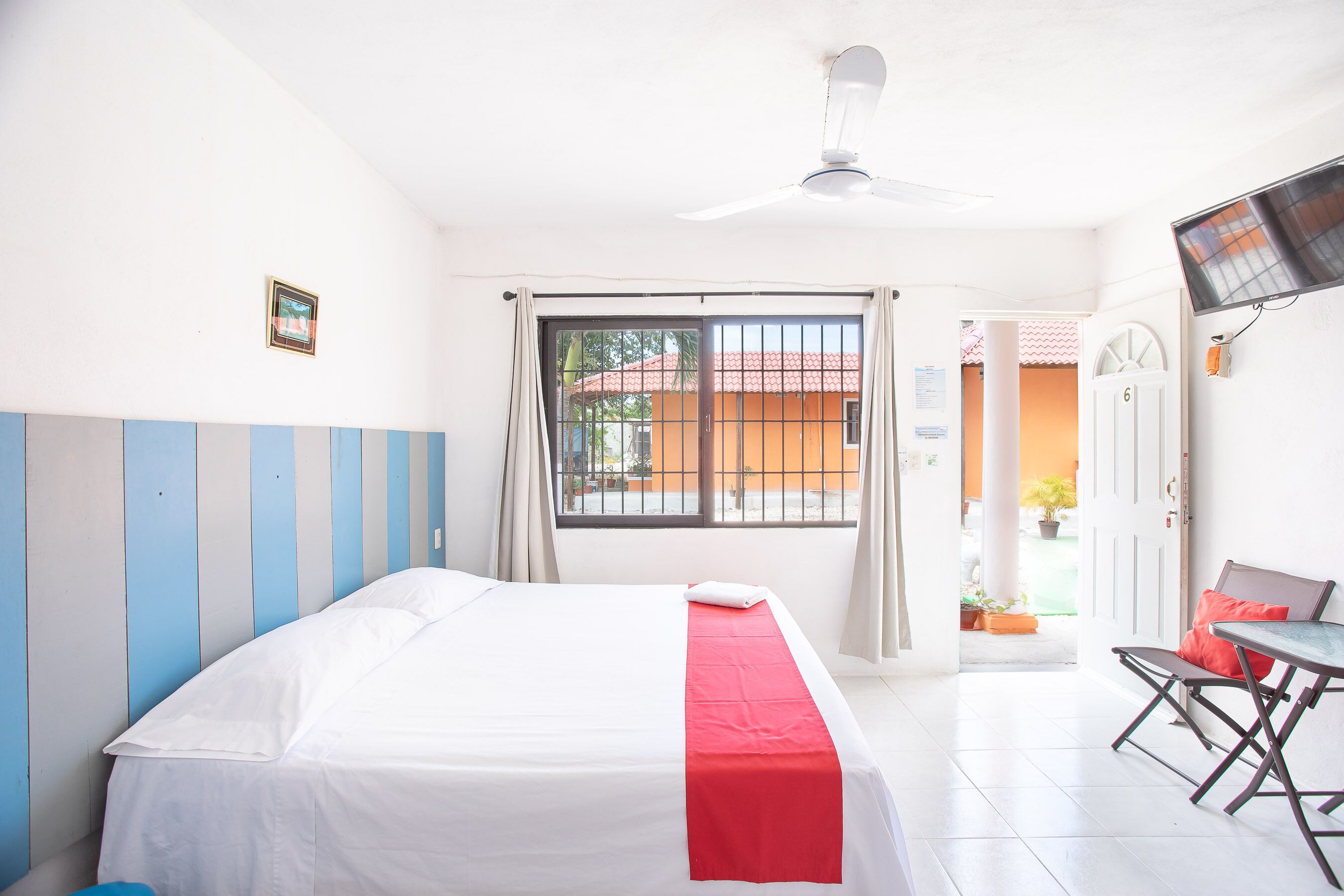 Habitación de hotel con cama, escritorio, silla, televisión y ventana con cortinas.