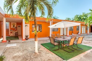 An outdoor patio area with a table and chairs, a palm tree, and a building with orange walls and a white door. - Hotel Casa Ariana (Bacalar)