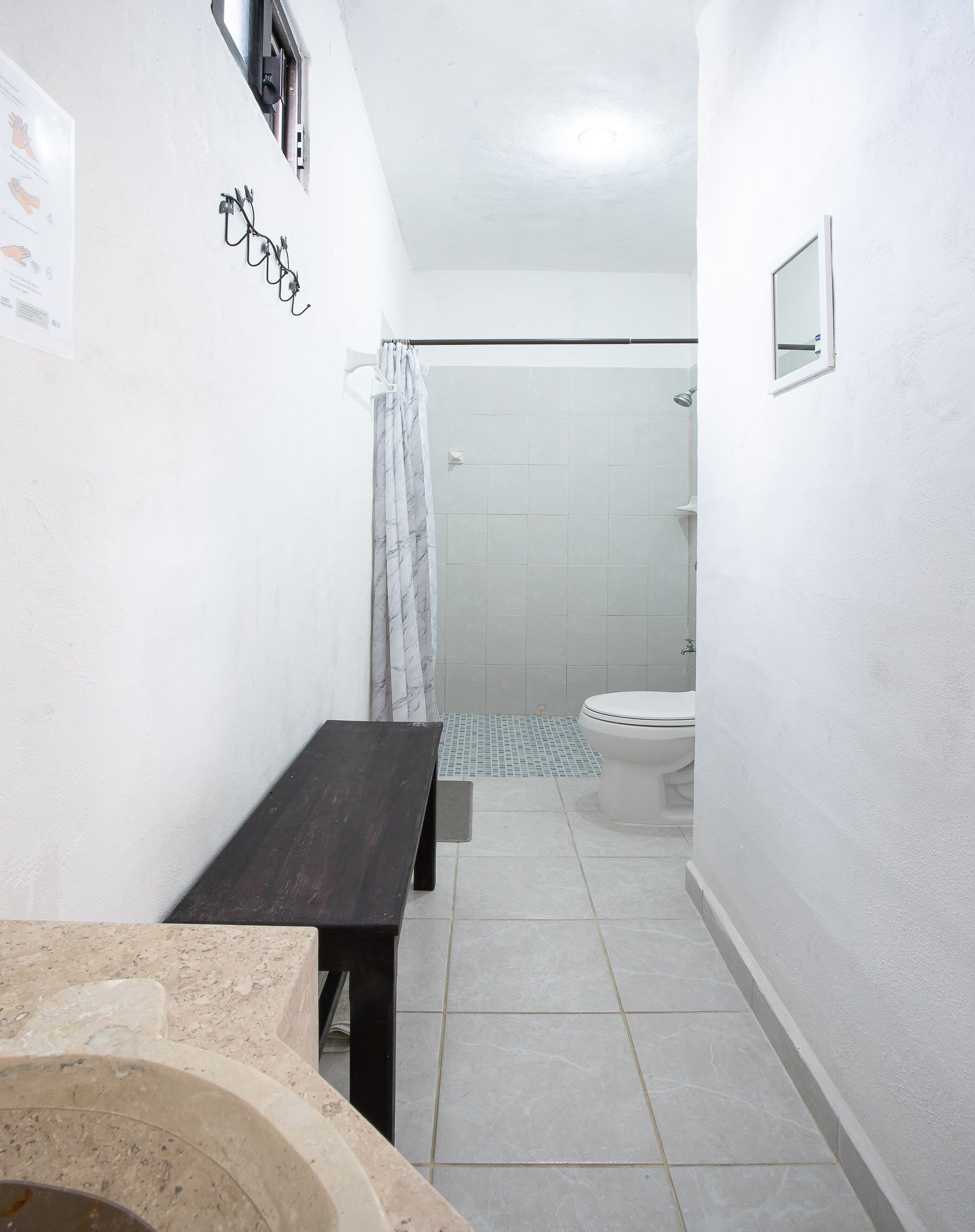 A narrow bathroom with a toilet, a shower, and a bench.