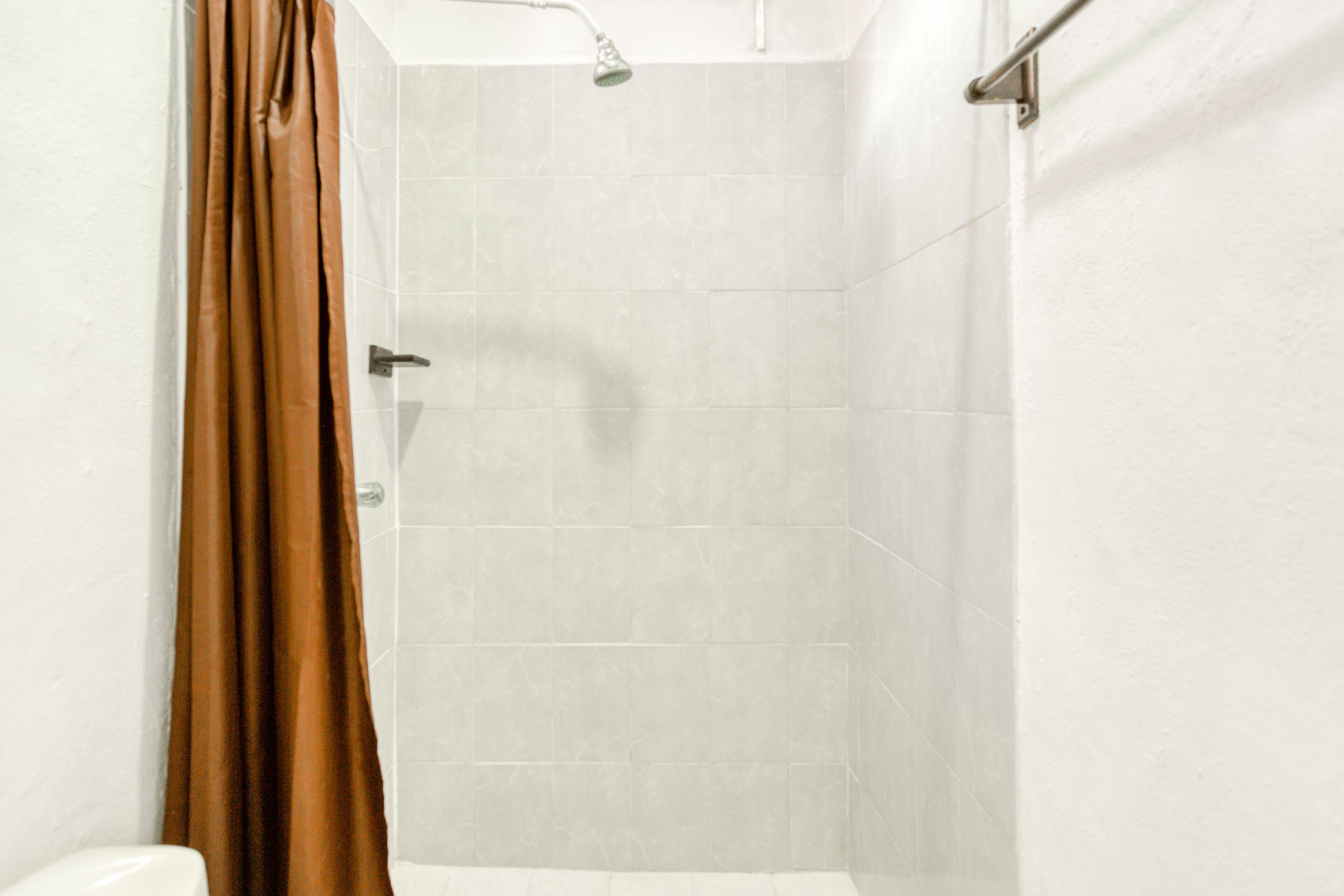A bathroom with white tiles, a shower with a brown curtain, and a visible showerhead.