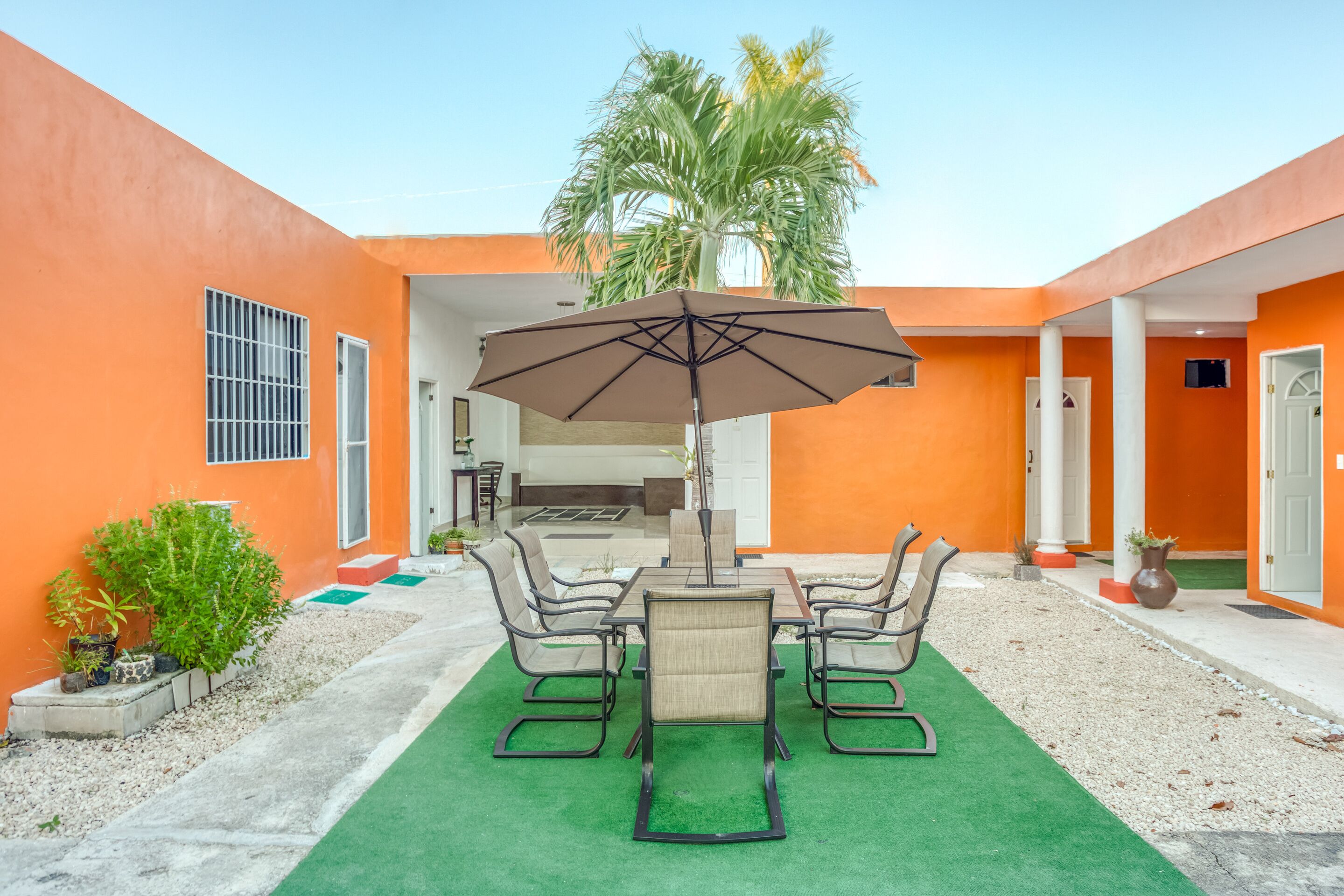 An outdoor patio with a table and chairs, a large umbrella, and a palm tree.