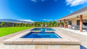 Una piscina con vistas a las montañas, un porche cubierto con mobiliario exterior y un césped cuidado.
