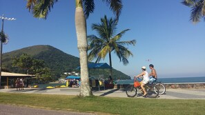 A beach scene with two cyclists, a kiosk, and a mountain in the background.