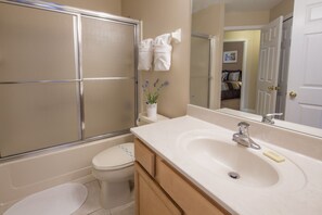 A bathroom with a shower, toilet, sink, and a mirror reflecting a bedroom. - Isle of Tranquility by VillaDirect (Kissimmee)