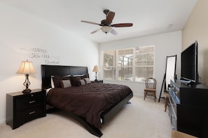 A bedroom with a bed, nightstands, a ceiling fan, a dresser, a television, and a window with blinds.