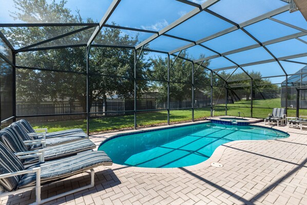 A covered outdoor swimming pool with lounge chairs and a hot tub.