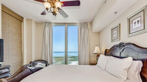 A hotel room with a large bed, a ceiling fan, a view of the beach, and a television. - Sunrise View~Nautical Themed & Family Friendly! (Pensacola Beach)