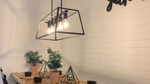 Een houten eettafel met zwarte stoelen, een hanglamp en een bord met de tekst 'gather' aan de muur.