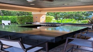 Een buitenkeuken met een groot eiland, barstoelen en een plafondventilator.