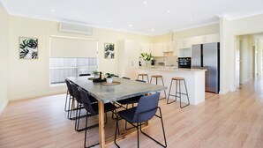 A modern kitchen with a central island, wooden flooring, and a dining area with chairs and a table. - Aldinga Beach Experience (Aldinga Beach)