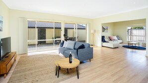 A spacious living room with a grey sofa, a wooden coffee table, and a TV on a wooden stand. - Aldinga Beach Experience (Aldinga Beach)