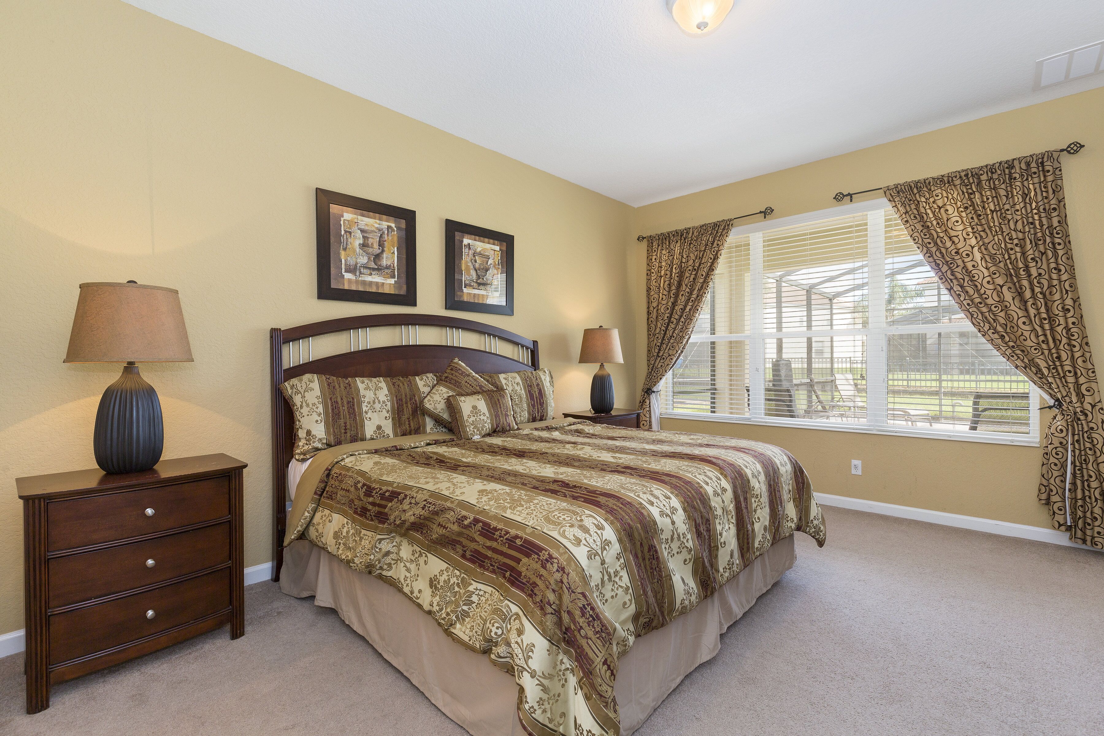 A bedroom with a large bed, two bedside lamps, a nightstand, and a window with curtains.