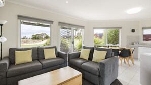 A modern living room with two grey sofas, a wooden coffee table, and large windows offering a view of the outdoors.