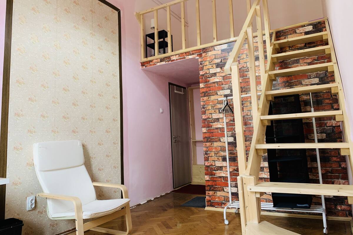 Una habitación con una silla de madera, un muro de ladrillo y una escalera de madera.