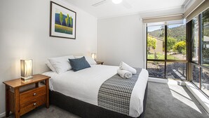 Un dormitorio con cama, mesitas de noche, ventilador de techo, ventana con vistas al exterior y un cuadro en la pared.