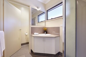 Un baño con un lavamanos blanco, un espejo encima y una ventana.