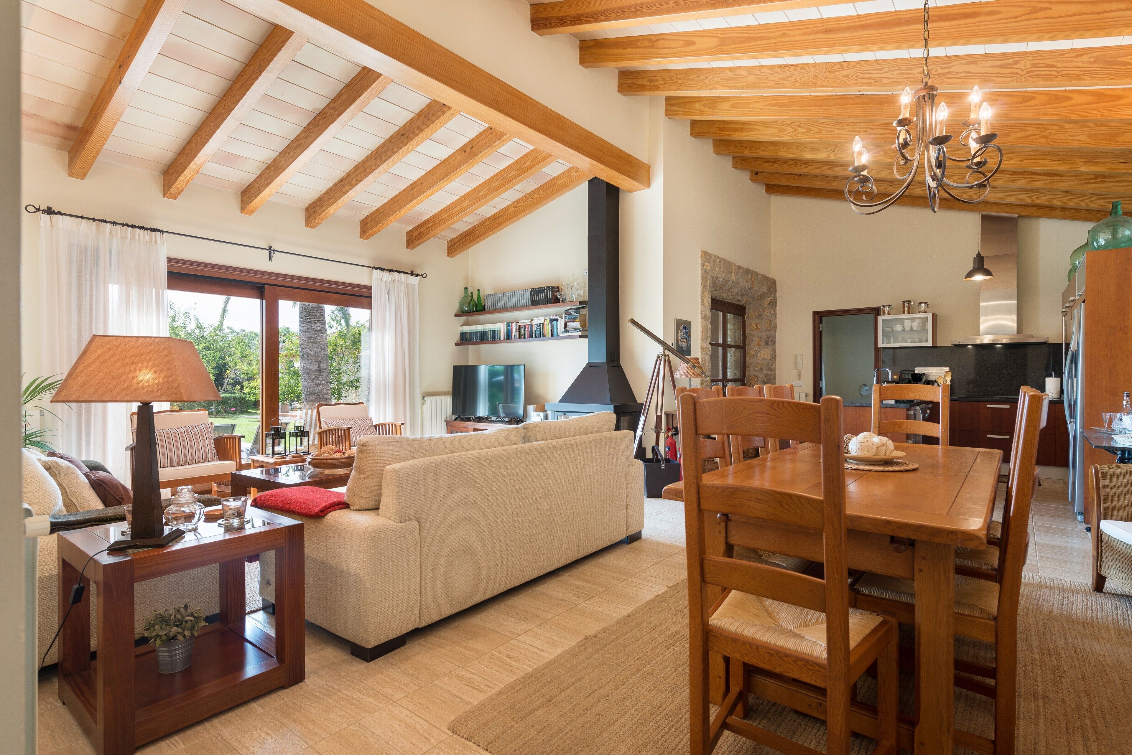 Un salón comedor amplio con techo de madera, un sofá, una mesa de comedor con sillas y una televisión.