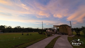 A covered outdoor area with a wooden structure, a paved walkway, and a grassy field.