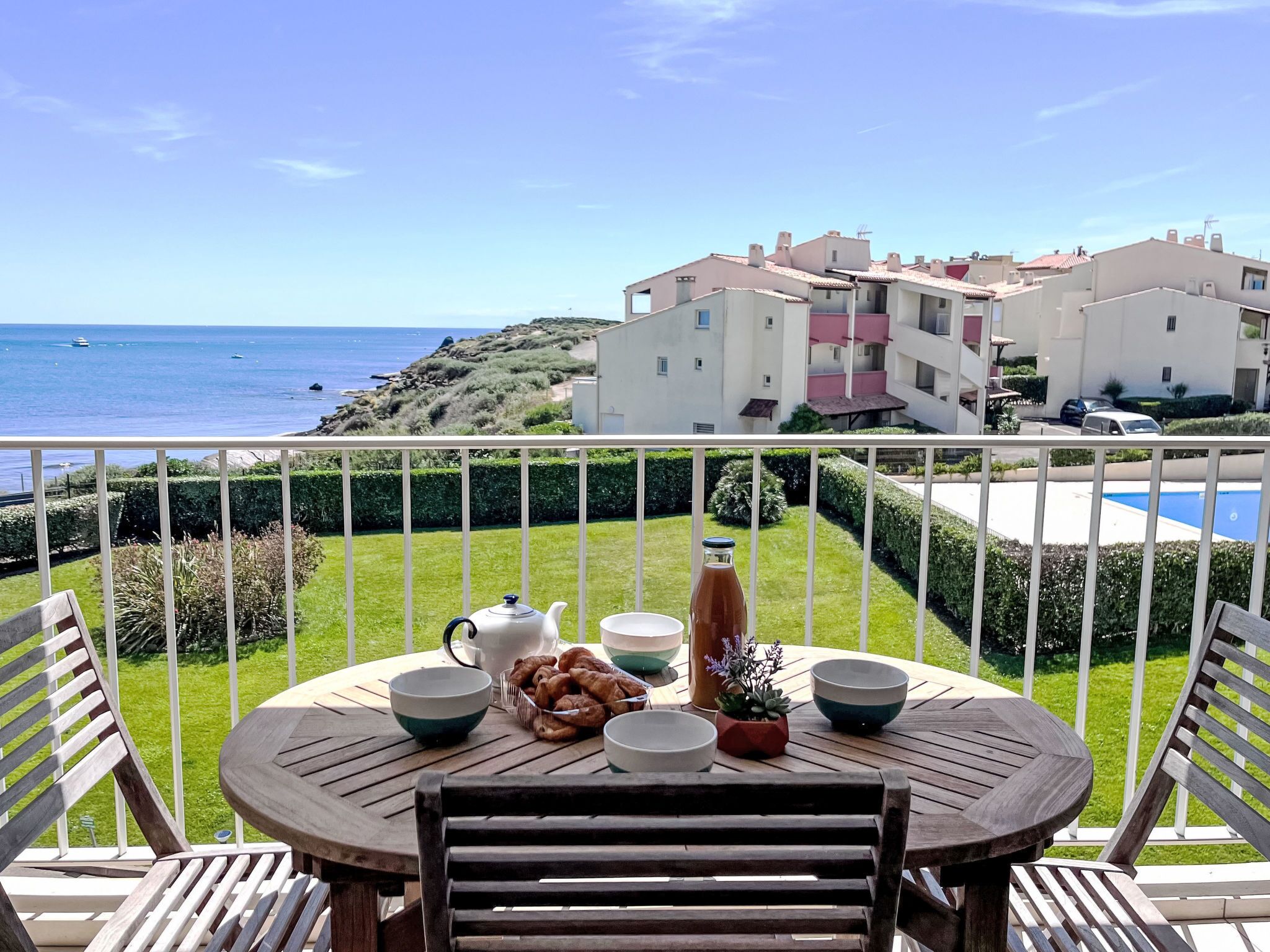Ein Balkon mit Frühstückstisch, der auf eine Küstenlandschaft mit Gebäuden und einem Swimmingpool blickt.