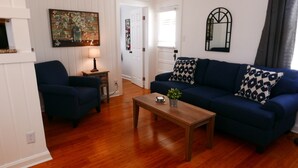 Sala de estar com sofá azul, mesa de centro de madeira, poltrona azul, mesa lateral com abajur e um quadro na parede.