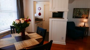 Uma sala de jantar com uma mesa posta para dois, um vaso de flores e uma cozinha ao fundo.