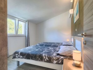 Ein Schlafzimmer mit einem Bett, einem Fenster und einem Nachttisch mit einer Lampe.