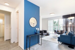 Een moderne woonkamer met een blauwe accentmuur, een ronde spiegel, een bank, een salontafel en een vloerlamp.