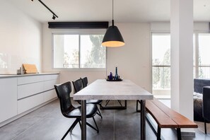 Une cuisine moderne avec un plan de travail en marbre, des chaises noires, un banc en bois et un luminaire suspendu.