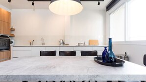 A modern kitchen with a marble island, black chairs, and a large pendant light. - Modern 2BR Apt w Private Parking in City Center (Ramat HaSharon)