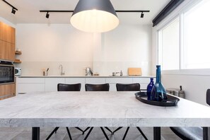 A modern kitchen with a marble island, black chairs, a large pendant light, and a window to the right.